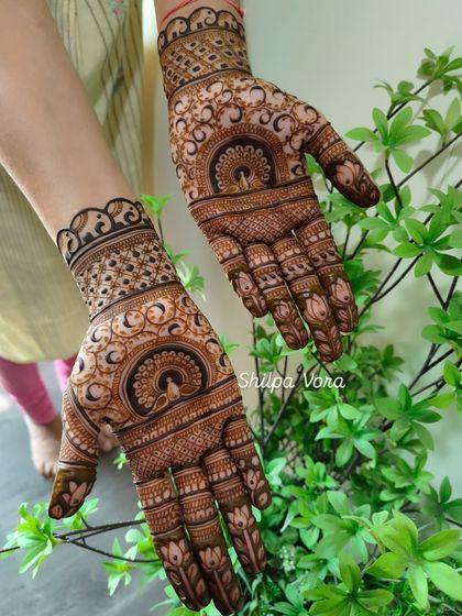 A full view of the peacock mandala design for Gangour, shown against a natural plant background.