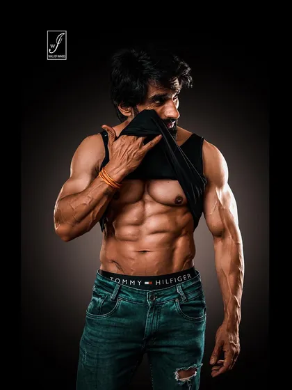 Using a tank top as a prop to frame the midsection, this shot draws immediate attention to the athlete's shredded six-pack abs. It's a confident and popular look for fitness influencers.