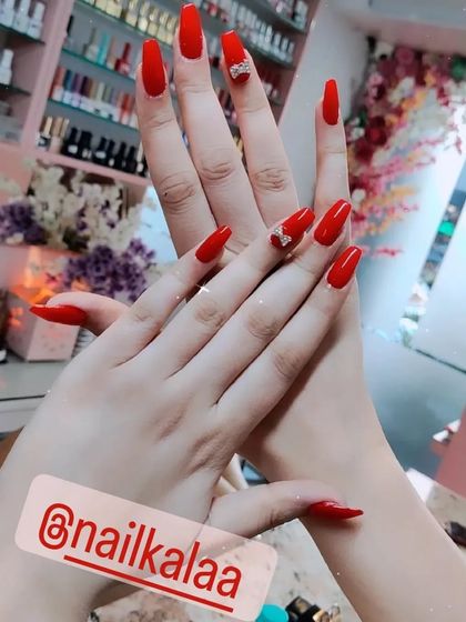 A classic, bold red manicure on long coffin nails, with a cute rhinestone bow accent.