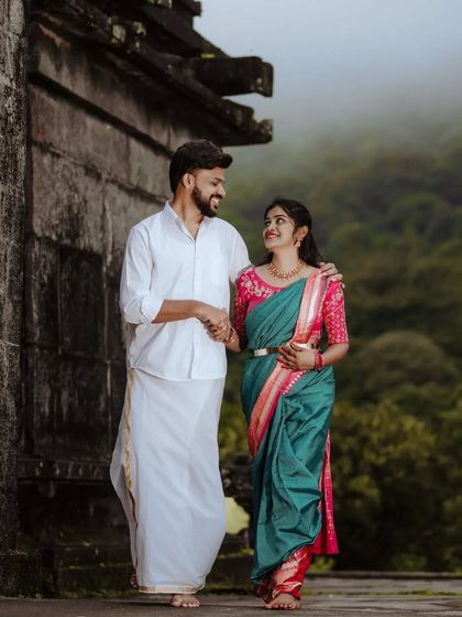 A couple in traditional attire walks together against a backdrop of lush green hills and an ancient temple, a perfect pre-wedding shot.