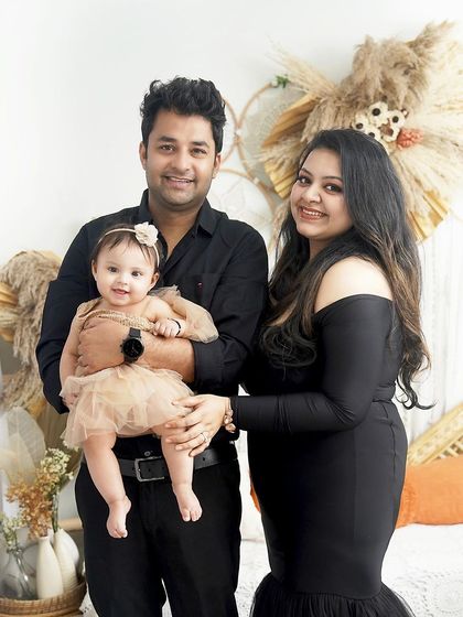 A classic family portrait with warm smiles. The coordinated black outfits and the baby's sweet expression make this a timeless keepsake.