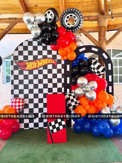 A Hot Wheels party with a checkered arch backdrop and balloons in the brand's signature orange and blue. The tire and flame details add to the excitement.