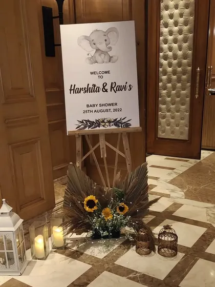 This is an example of a simple and elegant entrance for a boho-themed baby shower. The setup includes a personalized welcome sign, dried pampas grass, sunflowers, and lanterns to greet guests.
