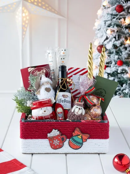 Bringing the magic of the holidays to life with a festive Christmas hamper. This box is filled with seasonal joy, including a miniature wine, snowman-themed treats, Lindt chocolates, and charming ornaments, all packed in a custom red and white box.