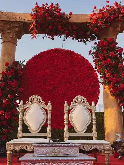 A close-up of the 'Jashn e Ishq' mandap, featuring a massive red rose backdrop and ornate silver chairs. The design is all about celebrating love with passion and grandeur.