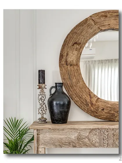 A close-up of a rustic console table, featuring a large, heavy-set wooden mirror. The distressed finish of the table and the simple black vase create a powerful, earthy vignette that speaks to timeless design.