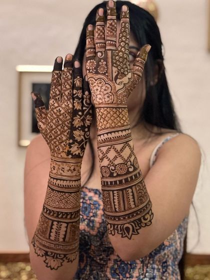 A bride peeking through her henna-adorned hands, a classic pose that highlights the beautiful back-of-hand design.