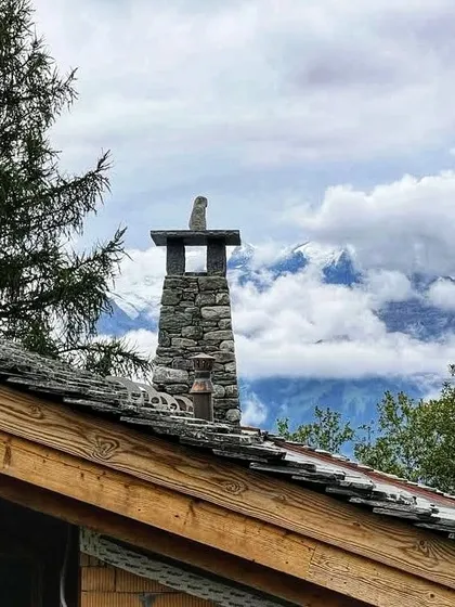 The stone chimney detail on our Verbier chalet, set against a backdrop of clouds and mountains. We believe in using local craftsmanship and materials to create details that are both beautiful and authentic to the location.