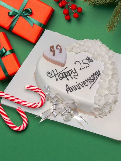 A heart-shaped 25th-anniversary cake, perfect for a Christmas-season celebration. The simple and elegant design is surrounded by festive decorations.