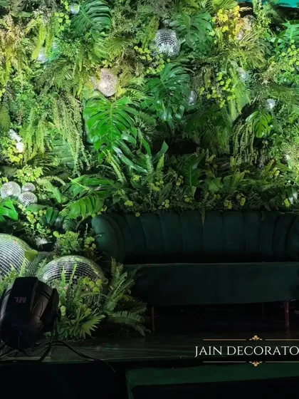 A photo spot that's an escape into a tropical disco. A lush wall of green foliage provides a rich backdrop for a velvet couch and scattered disco balls, creating a perfect corner for glamorous pictures.