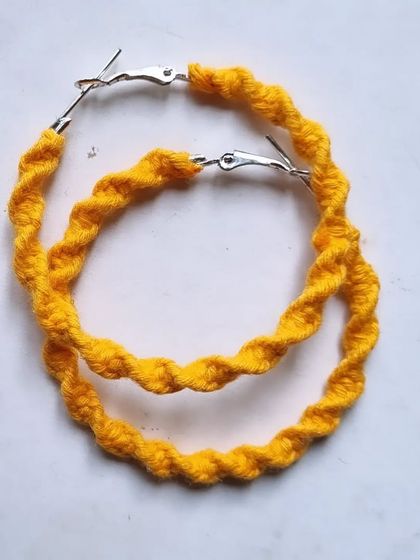 A pair of twisted macrame hoop earrings in yellow, offering a different texture and style.