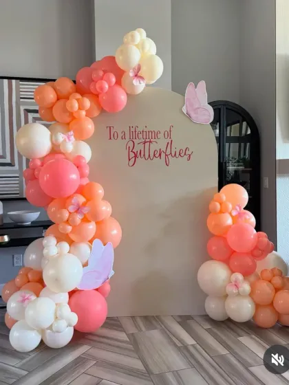 A soft, peachy-pink butterfly-themed balloon arch against a plain backdrop.