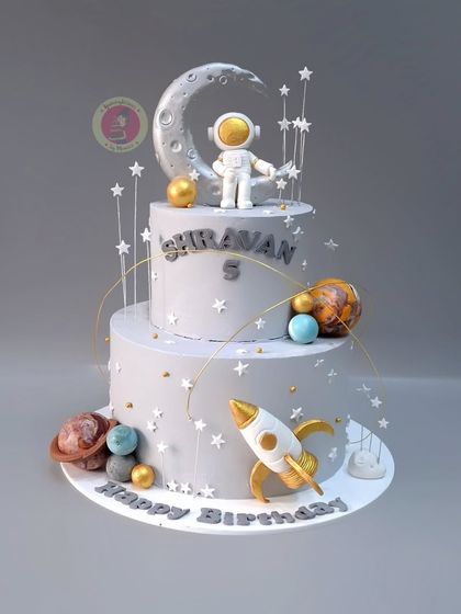 A dreamy space-themed cake in elegant grey and gold tones, with an astronaut, rocket, and planets.