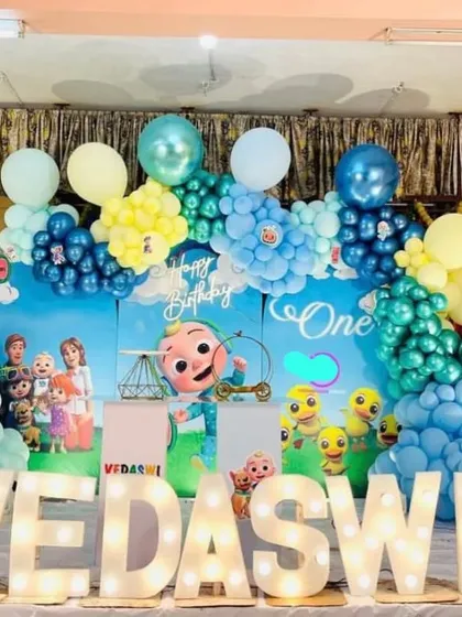 A Cocomelon first birthday party with large marquee letters. This decoration features a character backdrop and a colorful balloon arrangement.