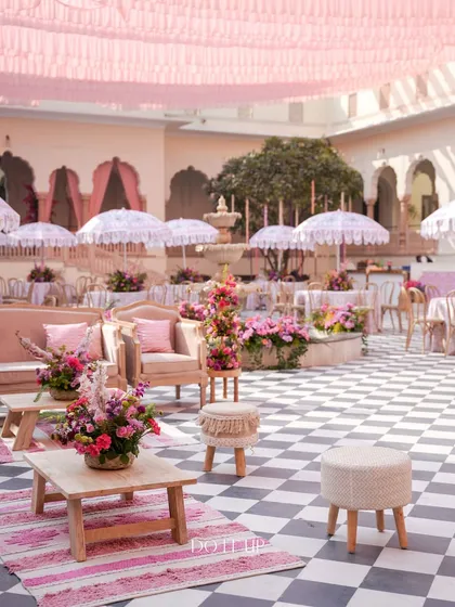A wide view of the lounge seating at the Jaipur welcome lunch. The checkered courtyard is filled with pink-toned furniture, patterned rugs, and floral arrangements, creating a cohesive and beautiful event space.