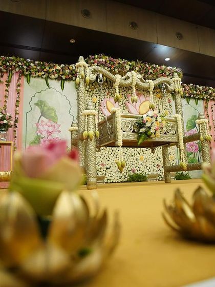 A low-angle shot of the naming ceremony stage, focusing on the brass lotus lamps in the foreground which add a warm, traditional glow to the setting.