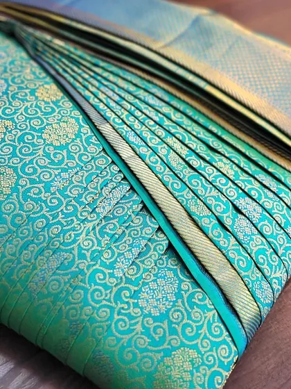 A stunning teal silk saree pre-pleated for a bride's reception. The pleats are set to create a beautiful fan effect, showcasing the saree's rich texture and design.