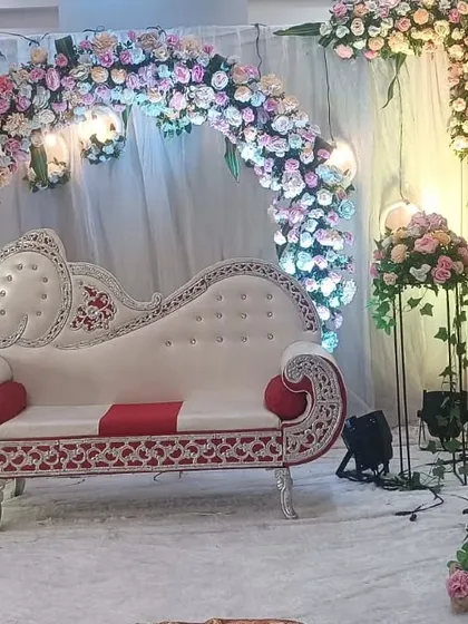A closer look at a floral engagement stage, highlighting the intricate arrangement of pastel roses on the circular arch. The elegant diwan sofa and spotlights create a perfect setting for the couple's special moments.