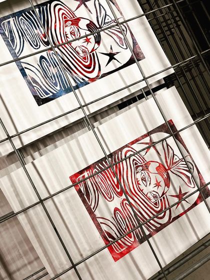 The finished linocut prints drying on a rack, showing variations in the ink application.