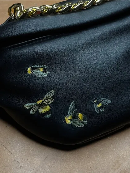 A cluster of realistic, fuzzy bumblebees hand-painted on a black leather bag.