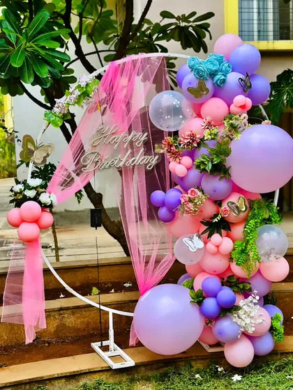 A beautiful outdoor birthday decoration with a circular frame, pink draping, and a lush arrangement of pink and purple balloons.