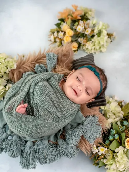 A sweet, sleepy smile from a baby wrapped in a green swaddle. The floral arrangement creates a beautiful frame, highlighting the baby's peaceful expression.
