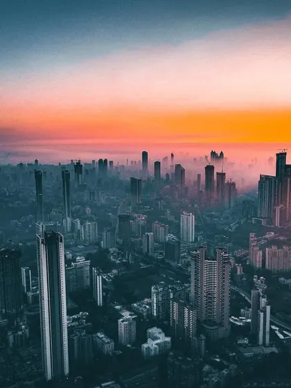 The sun sets over a hazy Mumbai skyline, with a strong color grade applied to give the scene an intense, apocalyptic feel.