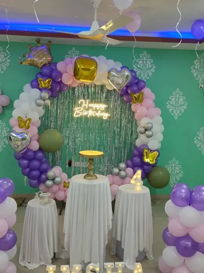 A purple, pink, and white balloon ring with a silver tinsel curtain and crown and butterfly accents.