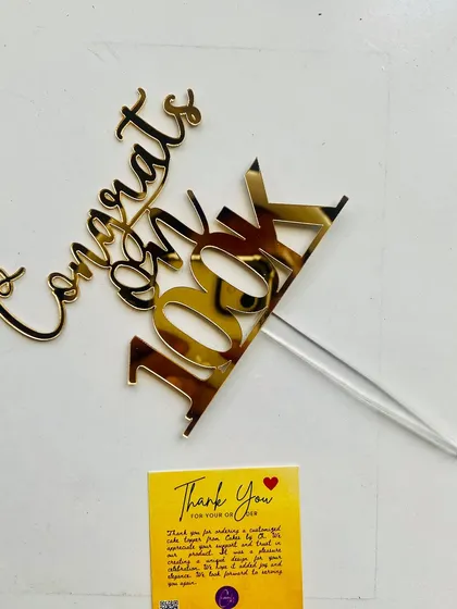A close-up of the "Congrats on 100K" topper with a thank you card, ready to mark a significant milestone.