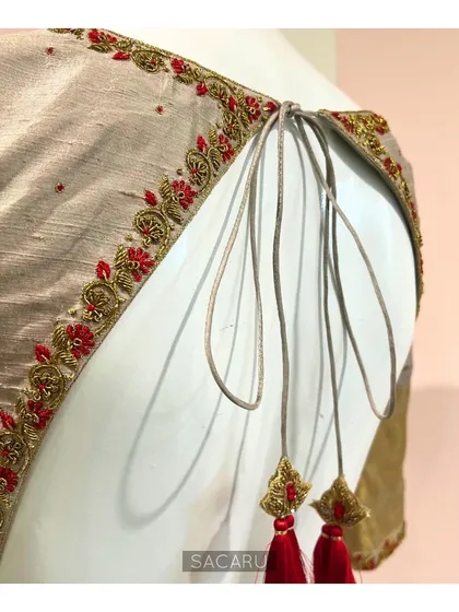 An elegant and traditional hand-embroidered Kanjeevaram saree blouse with a deep back opening, delicate tie-ups, and red tassels.