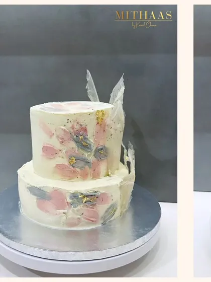 This two-tiered cake showcases a painterly effect, achieved by hand-painting the cocoa butter frosting with natural tints from berries. The abstract strokes of pink and grey, highlighted with gold leaf, create a unique, artistic finish.