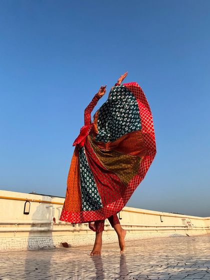 A celebration of flair and movement. The multi-colored 'anarkali' creates a stunning visual against the clear blue sky, concealing the dancer's form in a whirl of fabric.