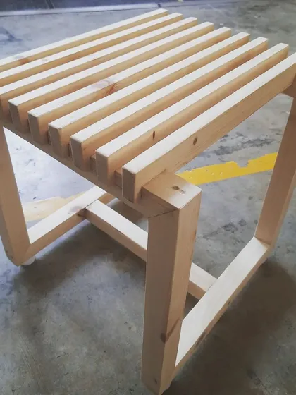 A profile view of the slatted stool, showing the joinery where the legs meet the frame.