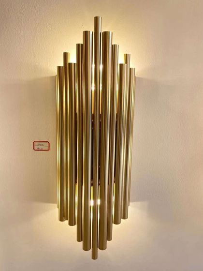 A striking wall sconce made of staggered brass tubes. This fixture creates a bold, architectural statement while providing beautiful ambient light.