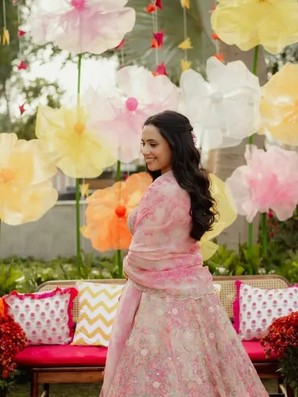 The bride posing against the colorful paper flower backdrop, her outfit perfectly coordinated with the pastel theme.