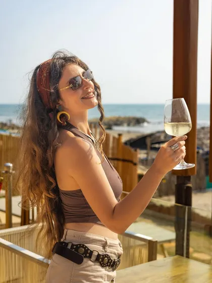 A model enjoying a glass of white wine with the ocean in the background. This is a classic aspirational lifestyle shot that connects the product with a feeling of luxury and relaxation.