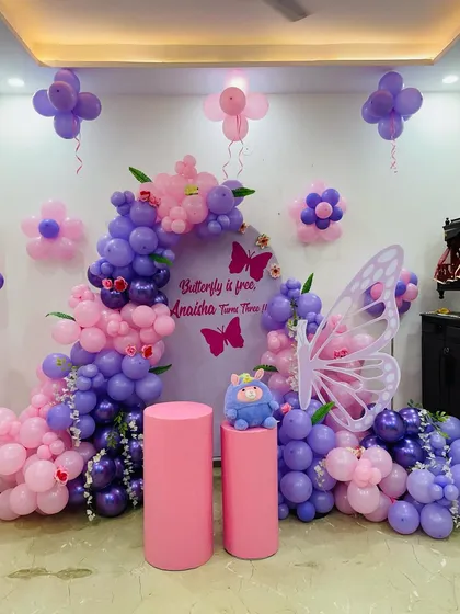 A full view of the whimsical butterfly-themed decoration for Anaisha's third birthday, showing the balloon arch, backdrop, and flower-shaped balloon clusters on the wall.
