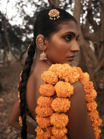 This shot introduces a garland of marigolds, a classic element in Indian culture, styled in a contemporary way. The close-up highlights the contrast between the flowers and the model's skin.