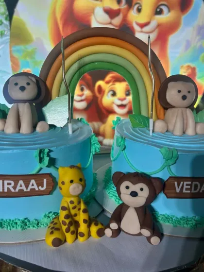 A closer look at the twin animal themed cakes, showing the personalized names and handcrafted fondant giraffe and monkey.