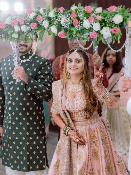 The bride's joyful entrance under the phoolon ki chadar, flashing a peace sign. Her personality shines through in this candid, happy moment.