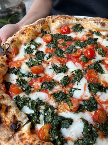 A close-up of the Spinach & Garlic pizza, showing the vibrant cherry tomatoes and wilted spinach.