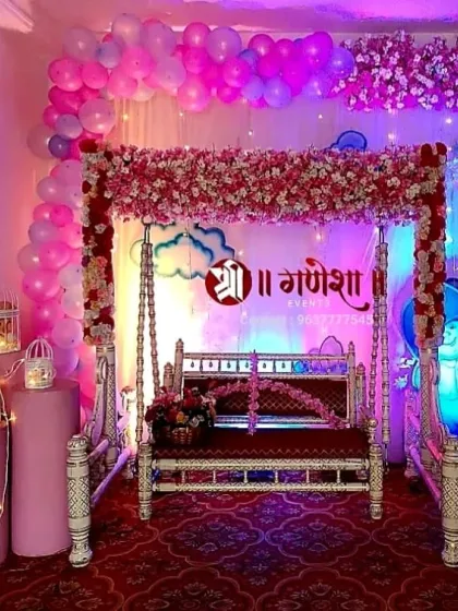 A modern and stylish baby shower decoration in pink and purple tones. This setup includes a flower-draped swing, balloon arrangements, and elegant lanterns to create a beautiful ambiance.