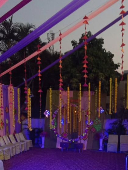 An evening view of an outdoor tent setup with purple and pink lighting. The colorful drapes and hanging decorations create a perfect party atmosphere.