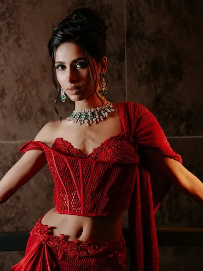 The corset is redefined in this ruby red pre-draped sari. The design merges the precision of a structured, boned corset with the fluid movement of a satin drape, shaping a new silhouette of tradition.