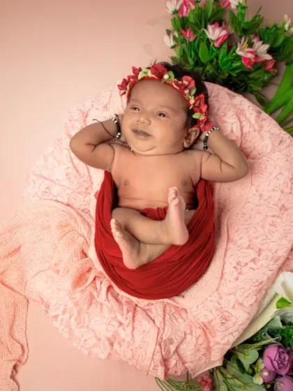 A happy little flower. This baby is relaxing in a nest of red and pink flowers, looking perfectly content and joyful.