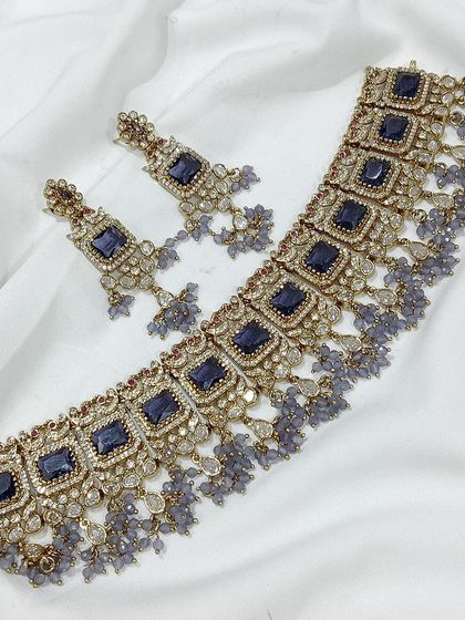 A popular choker design featuring square-cut stones, available in a variety of colors like emerald green, white, aqua blue, and baby pink. The matching earrings complete this elegant and modern ethnic set.