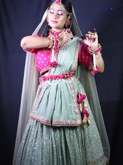 A client dressed for her Haldi or Mehendi ceremony in a mint green lehenga with a bright pink blouse, adorned with matching floral jewellery.