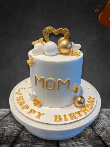 A classic and elegant birthday cake for Mom. The clean white fondant is accented with gold lettering, delicate hearts, and shimmering spheres, creating a sophisticated look for her special day.