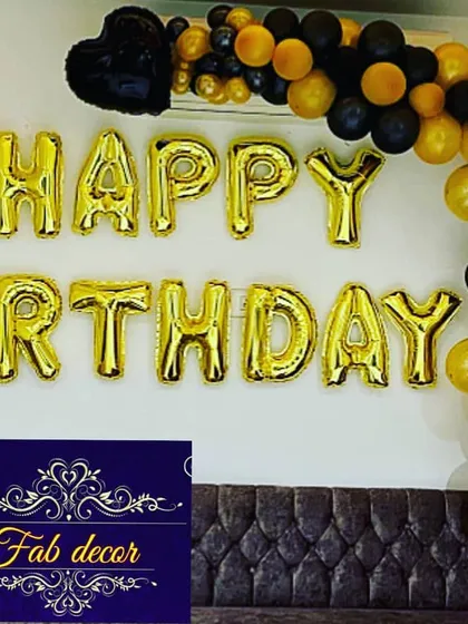 Even a simple decoration can make a big impact. This is a classic room decoration featuring 'HAPPY BIRTHDAY' foil letters on the wall, accented with a black and gold balloon garland. It's a great option for any budget.