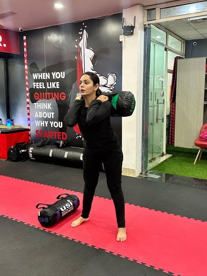 A student performs squats with a weighted bag, a functional exercise that builds power for takedowns and striking.